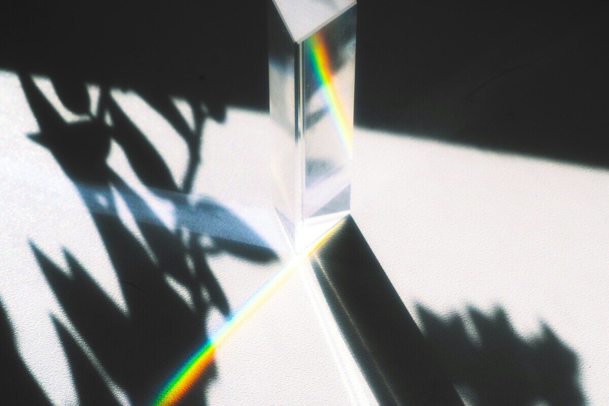 A glass prism splitting a beam of light into its colours against a bright wall