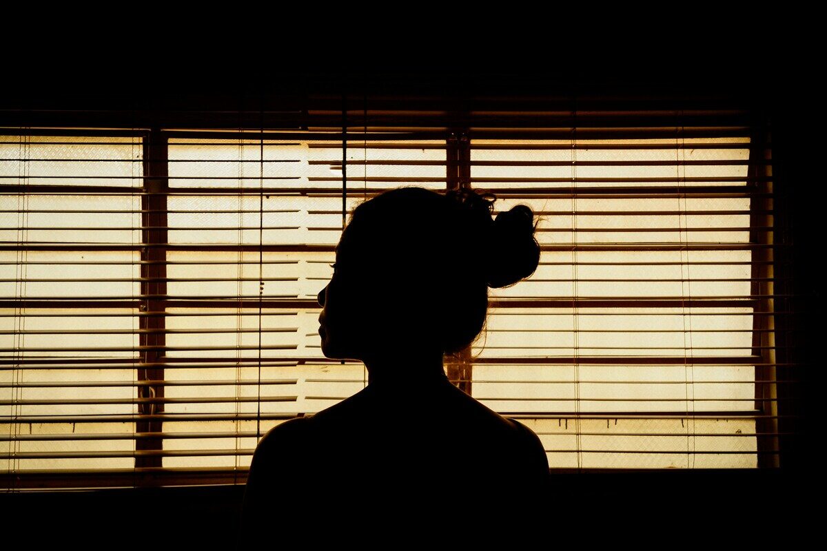 A person standing in silhouette in front of a sunlit venetian blind